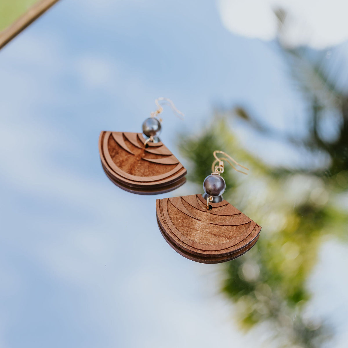 Wooden earrings with a reflective surface and blurred natural background